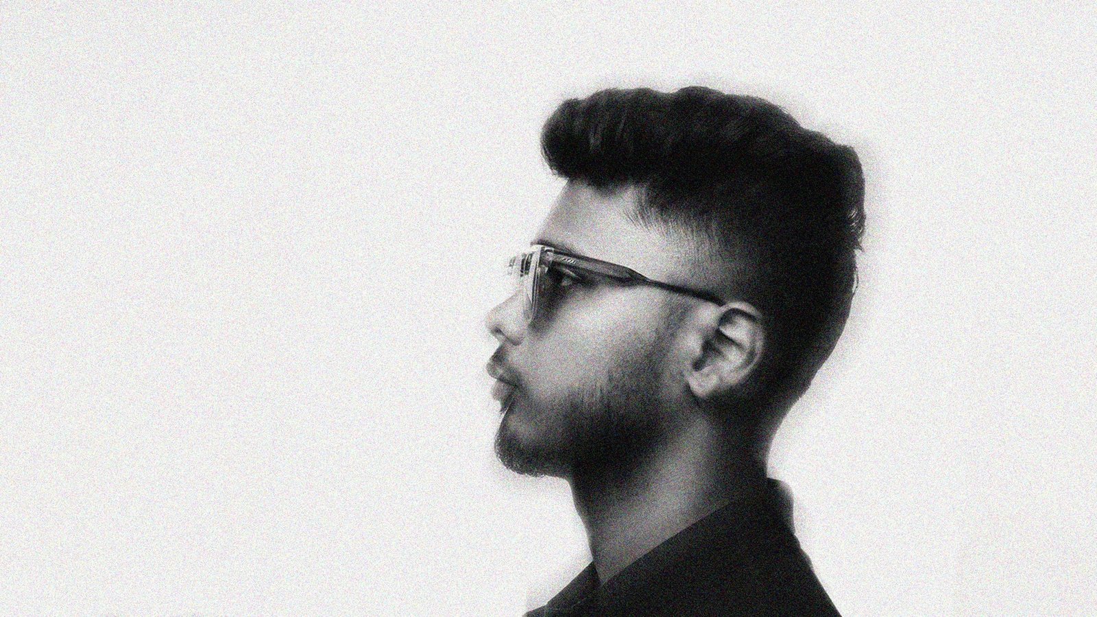 Noor Mohammad Fahim in profile, wearing clear-framed glasses — black and white portrait with film grain.